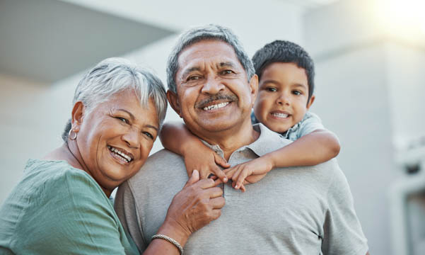 Grandpa, grandma and child hug with smile for happy holiday or weekend break with grandparents at the house. Portrait of elderly people holding grandchild on back for fun playful summer together.